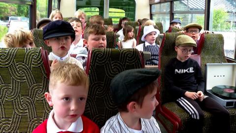 Clann òga a' seinn air bòrd seann bhus Mhic a' Bhriuthain