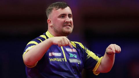 Luke Littler gesturing to the crowd that he is not going anywhere after winning a crucial leg against Jermaine Wattimena.