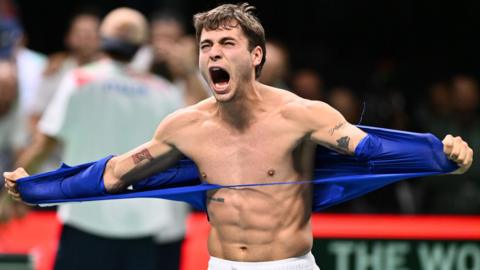 Flavio Cobolli tears off his T-shirt in celebration after sending Italy into the Davis Cup final