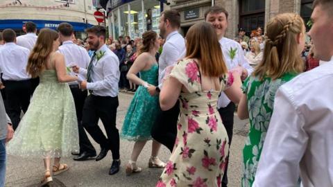 women in dresses and men in smart trousers and white shirts dancng

