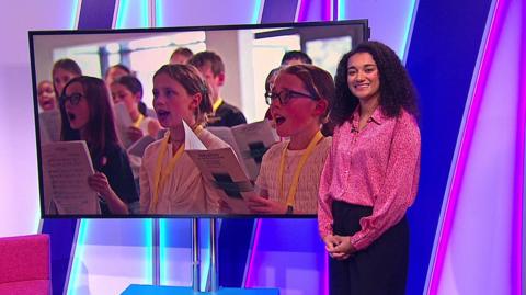 Nina in the studio with children singing in the screen