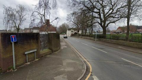 A Google street view image of a road going past a school with a the boundary fence and wall visible on the right. On the left is a wall with a dead end sign and a street sign which says "union street".