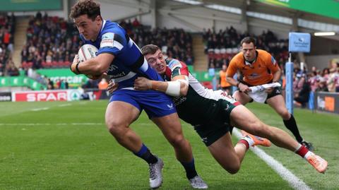 Leicester wing Adam Radwan tackles Bath's Henry Arundell from behind as the assistant referee looks on closely.