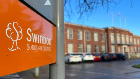 An orange Swindon Borough Council sign with the council buildings behind in the background