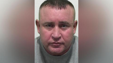 Mugshot of a man with short dark hair and a flushed face.