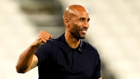Huddersfield Town manager Lee Grant wears a navy polo shirt and punches the air smiling