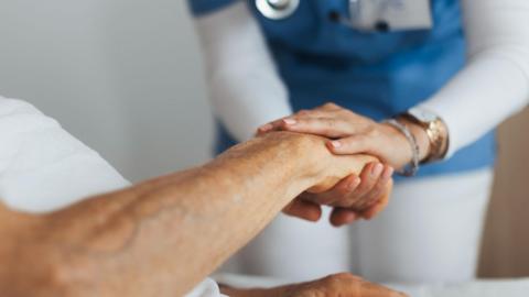 Close-up of caregiver holding senior client hand.