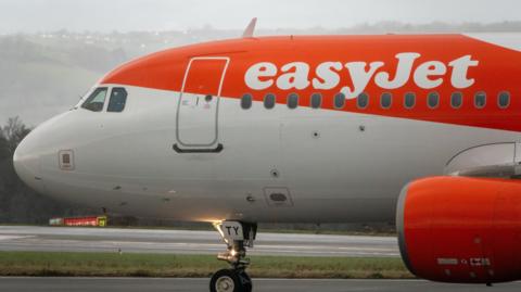An EasyJet flight. The plane is orange and white. It's on tarmac at an airport. 