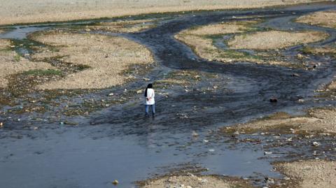 A woman stands by an almost entirely dried out river in Tehran that was once full