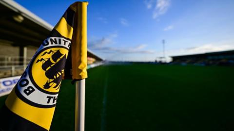 The Boston United club badge is showing on the corner flag at the Jakemans Community Stadium which can be seen in the background.