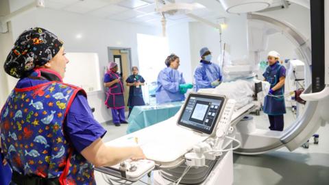 Hospital staff in surgical scrubs operating medical equipment.