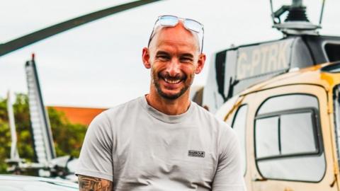 A man with a grey t shirt and no hair with sunglasses on his head