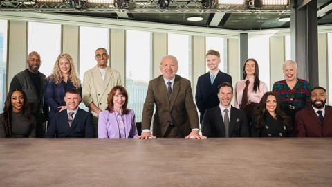 Lord Sugar in a boardroom surrounded by The Celebrity Apprentice contestants