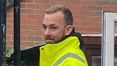 Steve Figg has short blond hair and is wearing a hi-vis jacket during an outdoor building project.
