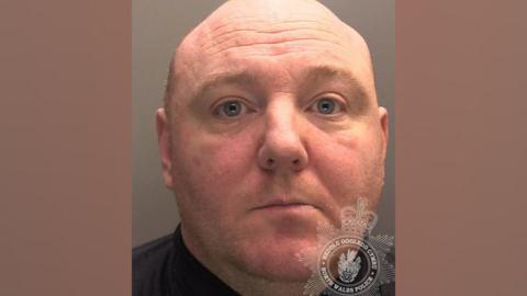 Anthony Saunderson's custody mugshot. He is bald with blue/grey eyes and light-coloured short stubble. He is photographed wearing a black shirt.