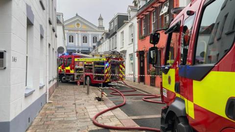 Two fire engines at the scene of the blaze in Jersey. A cordon is in place. A Methodist church can be seen at the end of the road.