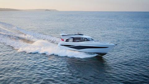 A white yacht with black stripes is seen on the water. There is a trail of whitewash behind it. 