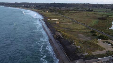 Waves crash into the coast of Jersey on a gloomy day. Fields are dotted along the coastline.