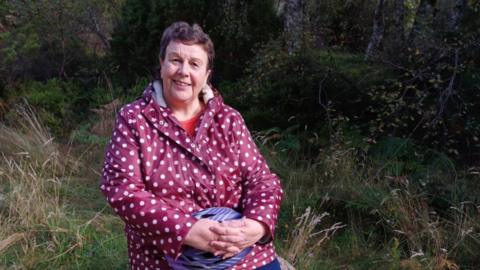 A woman wearing a polka dot jacket sits outside on a log