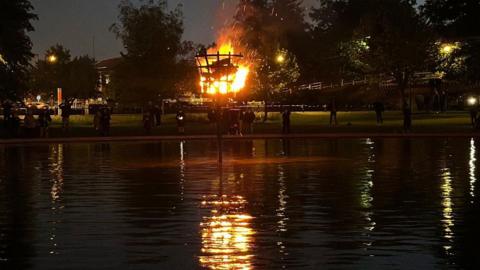 A flaming beacon reflected in the water in darkness.