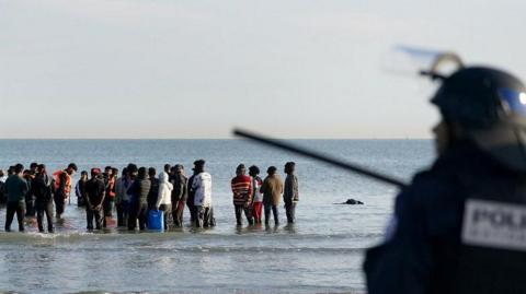 People thought to be migrants wade through the sea to board a small boat leaving the beach at Gravelines, France, in an attempt to reach the UK by crossing the English Channel.