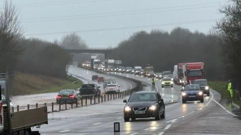 Flooding on the A30 near Ottery St Mary. There are cars and long tailbacks on the left side of the road, and cars in flood water on the opposite side.