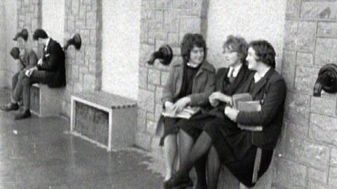 Black and white image of people sitting outside the new public toilets.  Taps can be seen on either side.