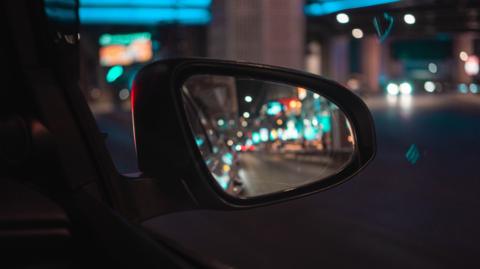 Close up of a car side mirror with a blurred street full of lights visible at night time