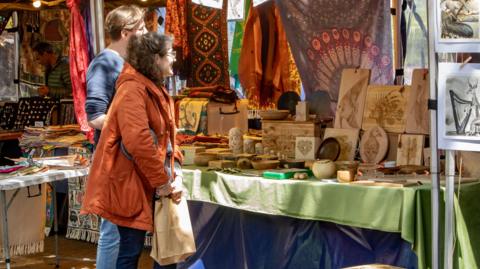 A man and a woman stand in front of a stall where wooden ornaments are displayed