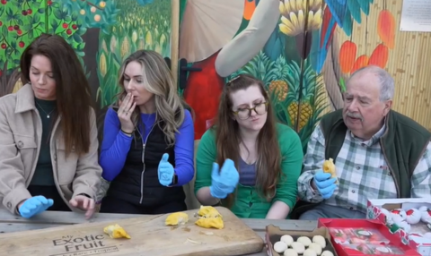 Three women and one man trying the expensive melon. They are all displaying different expressions
