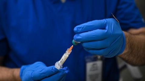 File image of a pair of hands carrying a syringe filled with measles vaccine