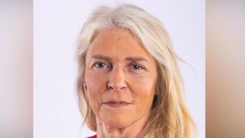 Lisa has long blonde hair and is smiling at the camera in this head and shoulders image. She has a red top on.