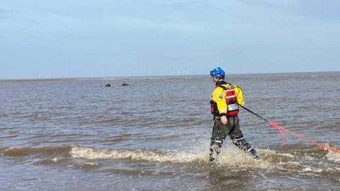 A coastguard officer is tied to a safety rope as he wades out to rescue the stranded walkers.