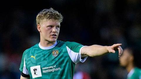 Scott Robertson playing for Notts County with his left arm raised as he points to something.