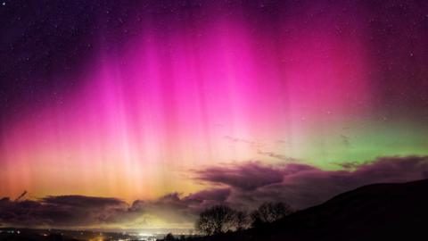 bright pinks in the night sky of the aurora. Some cloud on the horizon with a green tinge behind the cloud.