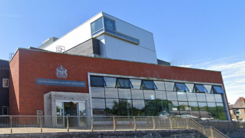 A four-storey court building - a rectangular red-brick building featuring a large section of broad glass windows to the right and a modern porch-style entrance on the left.