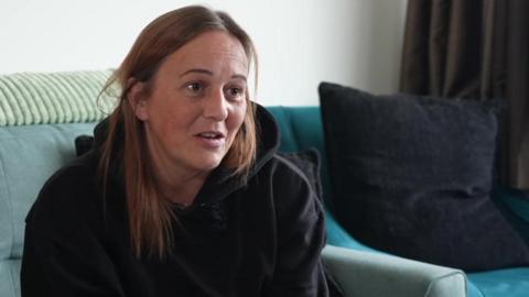 Tanya Matthews wears a black hoodie sitting on a blue sofa with a blue cushion.