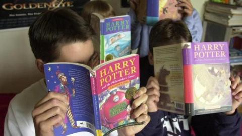 Children reading different Harry Potter books, which they are holding in front of their faces.