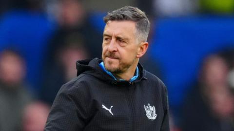 Port Vale boss Jon Brady walks to the dressing room wearing his club hoodie