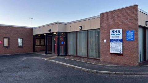 A brick built hospital with tarmac outside and an NHS Borders sign on the side