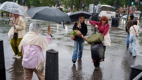A rainy city street scene with people holding umbrellas as they cross the road.