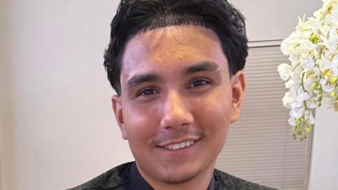 A smiling young man stood in a room.
