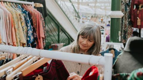 A woman shops for clothing in a sunny indoor market - stock photo