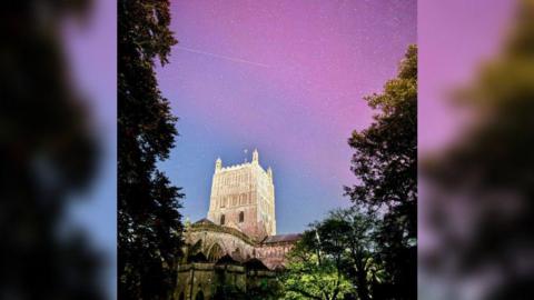 Tewkesbury Abbey framed by trees either side and the purple colours of the Northern Lights in the nightsky beyond