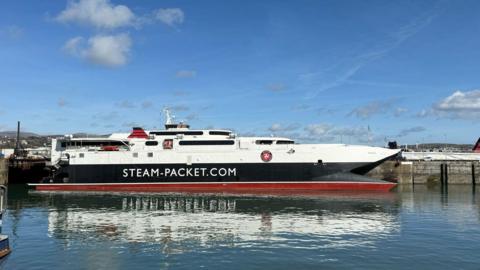 A closeup of the Manannan in the sunshine at Douglas Harbour, the sleek catamaran is white, navy and red withh writing that reads Steam Packet.