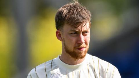 A photo of footballer Jasper Moon playing for Burton Albion Football Club in a stadium while wearing a white shirt with gold vertical lines, looking to his left