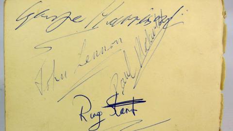 The signatures of the four members of The Beatles in blue ink on yellow paper.