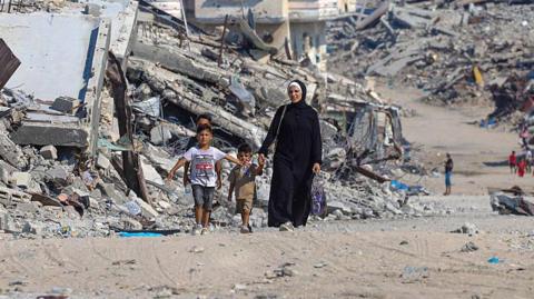 A Palestinian woman walks with children along a path lined with piles of rubble in the Sheikh Radwan neighbourhood of Gaza City