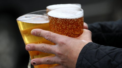 Three full drink glasses being held in the hands of someone wearing black. The dark background is blurred.