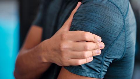 Man wearing a blue shirt grabbing at shoulder in pain.